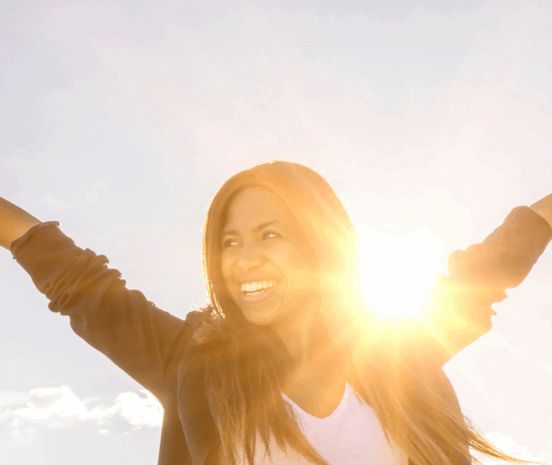 Sun shining over shoulder of woman cheering and smiling